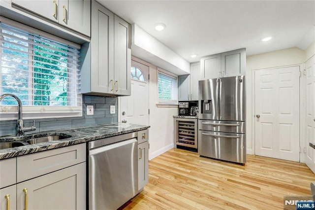 kitchen featuring appliances with stainless steel finishes, wine cooler, baseboards, dark stone counters, and light wood-style floors