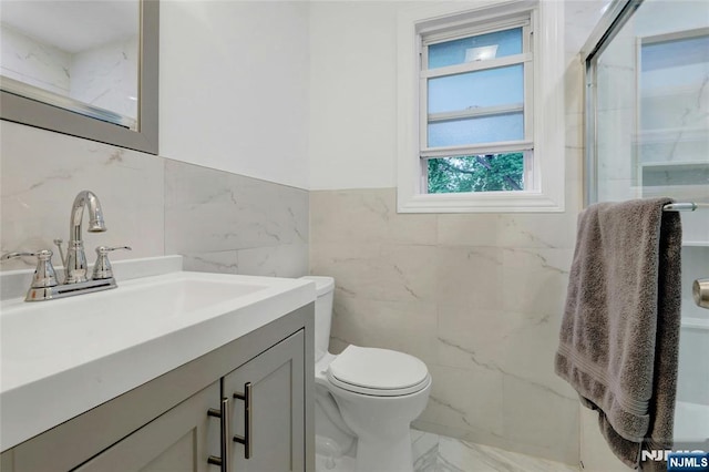 bathroom with tile walls, marble finish floors, a marble finish shower, vanity, and toilet
