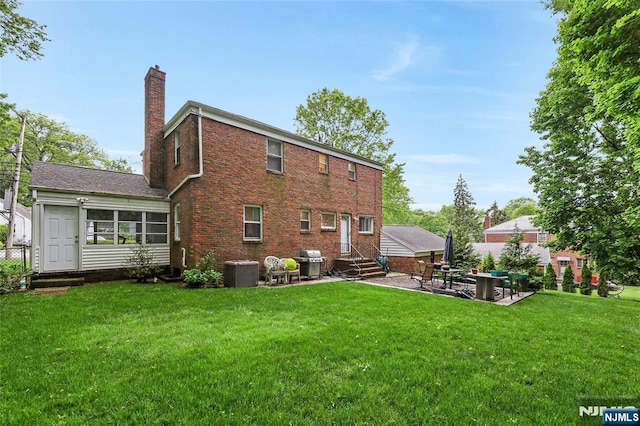 rear view of house with a chimney, entry steps, central AC, a patio area, and a yard