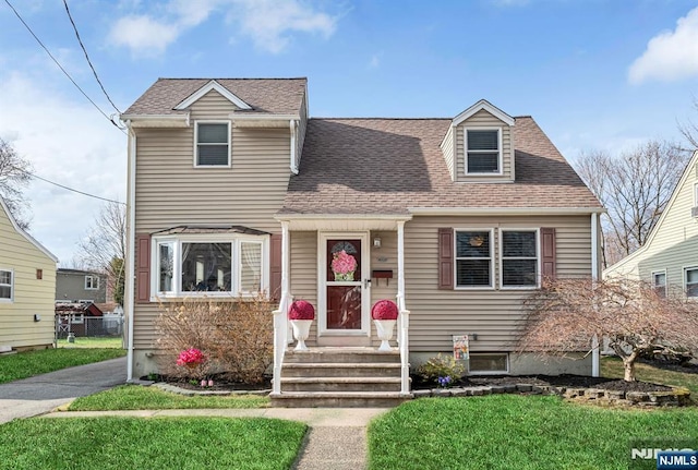 new england style home with a shingled roof and a front lawn