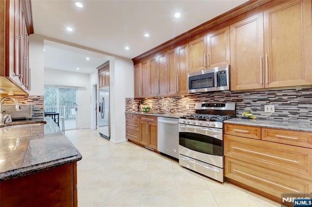 kitchen featuring recessed lighting, stainless steel appliances, backsplash, a sink, and dark stone counters