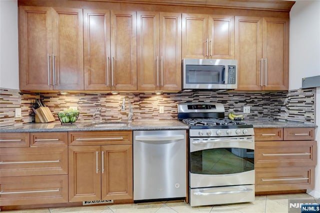 kitchen with stainless steel appliances, a sink, tasteful backsplash, light stone countertops, and light tile patterned floors