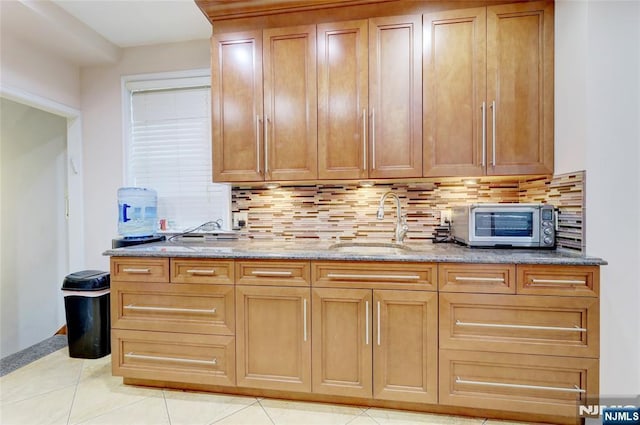 kitchen featuring backsplash, light tile patterned floors, light stone counters, and a sink
