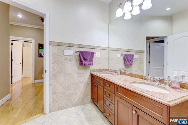 full bath featuring crown molding, a sink, tile walls, a wainscoted wall, and double vanity