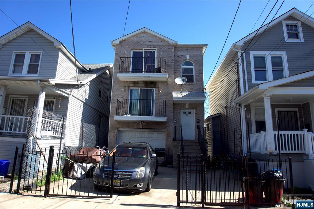23 Edwin Pl, Newark, NJ 07112 - view of front facade with brick siding, an attached garage, a fenced front yard, and concrete driveway