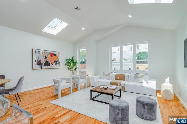 living room featuring visible vents, baseboards, lofted ceiling with skylight, and wood finished floors