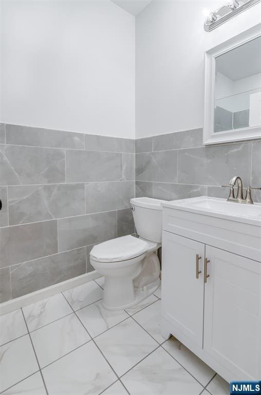 bathroom with vanity, marble finish floor, tile walls, and toilet