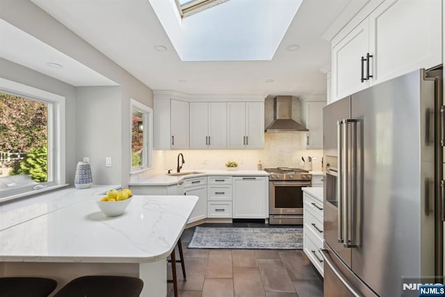 kitchen featuring wall chimney range hood, light stone counters, high quality appliances, white cabinets, and backsplash
