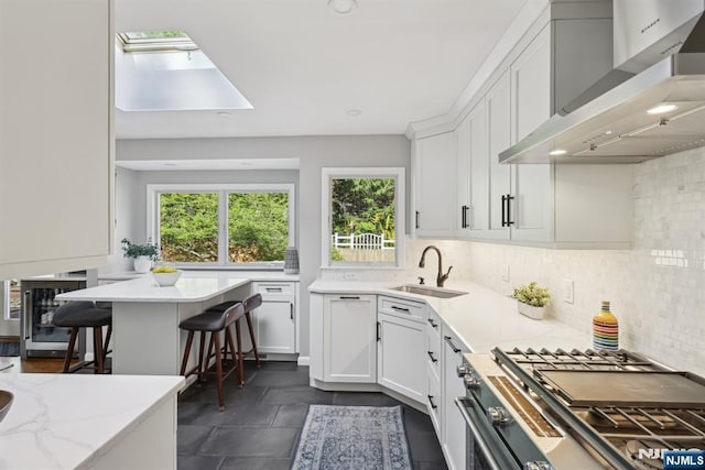 kitchen featuring high end stainless steel range oven, a sink, white cabinetry, and wall chimney range hood
