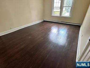 empty room featuring baseboards, baseboard heating, and dark wood-style flooring