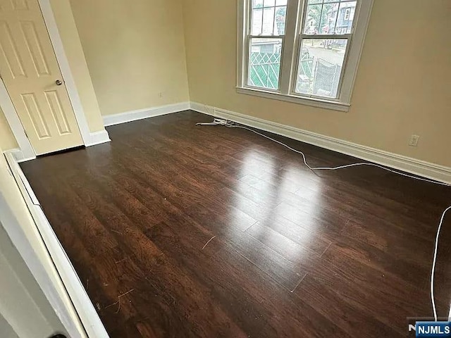 unfurnished room with dark wood finished floors and baseboards
