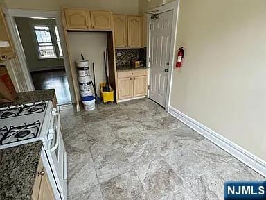 kitchen featuring dark stone counters, light brown cabinetry, backsplash, baseboards, and gas range gas stove
