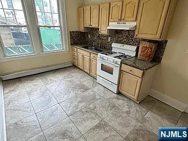 kitchen featuring backsplash, baseboard heating, white range with gas stovetop, light brown cabinets, and under cabinet range hood