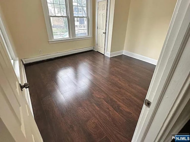 unfurnished room featuring a baseboard heating unit, baseboards, and dark wood-style floors