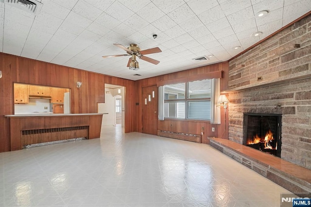 unfurnished living room featuring visible vents, radiator, ceiling fan, and a stone fireplace