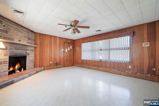 unfurnished living room with ceiling fan, tile patterned floors, wood walls, a stone fireplace, and visible vents