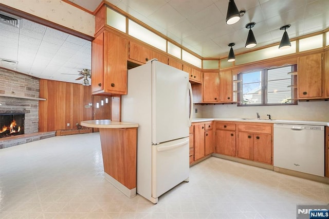 kitchen featuring brown cabinets, white appliances, light countertops, a stone fireplace, and light floors