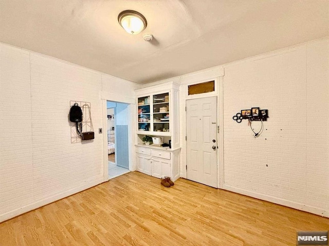 entryway with brick wall and light wood-type flooring