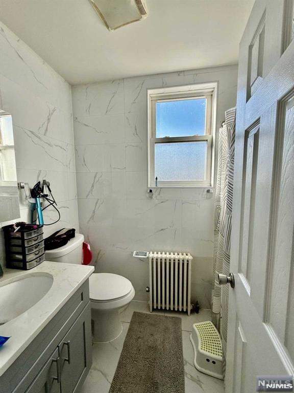 full bath with radiator heating unit, vanity, marble finish floor, and toilet