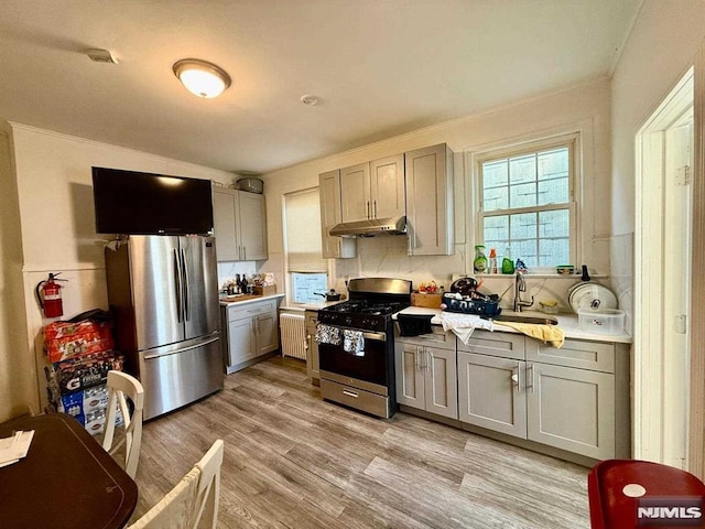 kitchen with light countertops, under cabinet range hood, gray cabinetry, stainless steel appliances, and light wood-style flooring