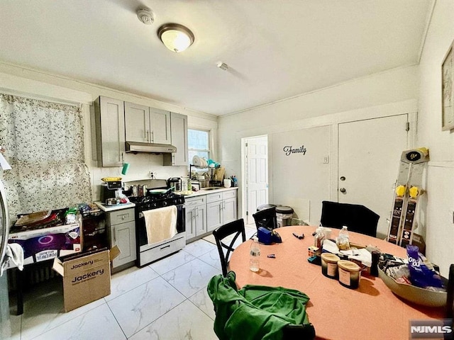 kitchen featuring gas range, light countertops, under cabinet range hood, gray cabinets, and marble finish floor