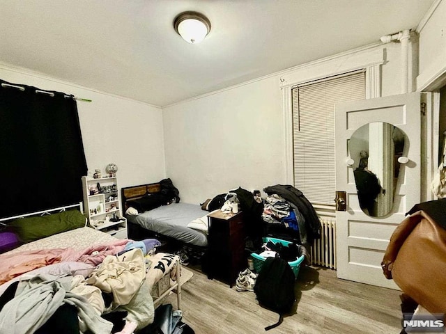 bedroom featuring light wood-type flooring, radiator heating unit, and ornamental molding