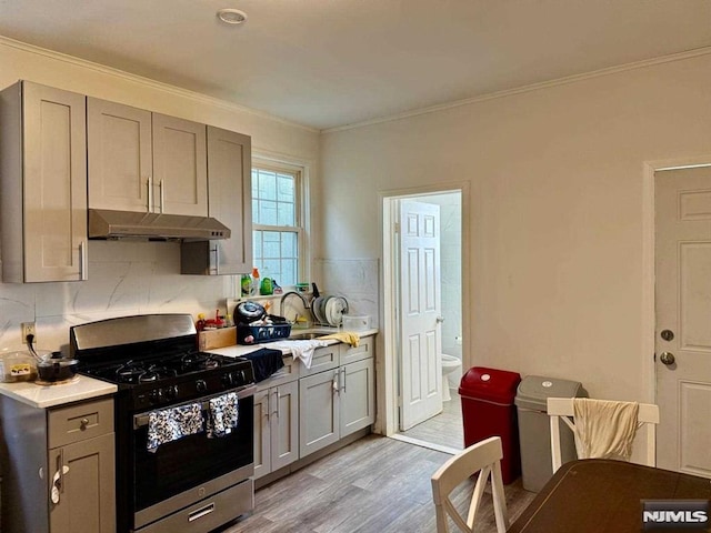 kitchen featuring gray cabinetry, gas range, a sink, and under cabinet range hood