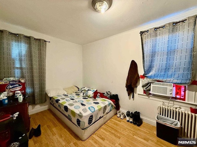 bedroom with radiator heating unit, cooling unit, crown molding, and wood finished floors