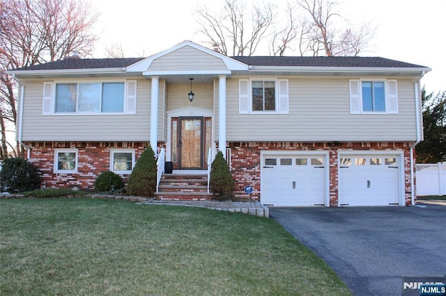 raised ranch with a garage, aphalt driveway, fence, brick siding, and a front lawn
