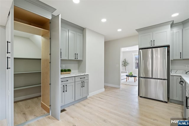 kitchen with light stone countertops, light wood-style flooring, freestanding refrigerator, and gray cabinets