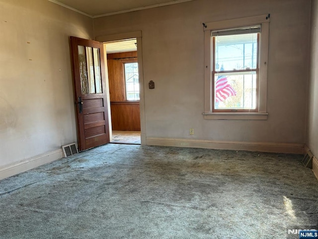 empty room with baseboards, visible vents, carpet floors, and ornamental molding