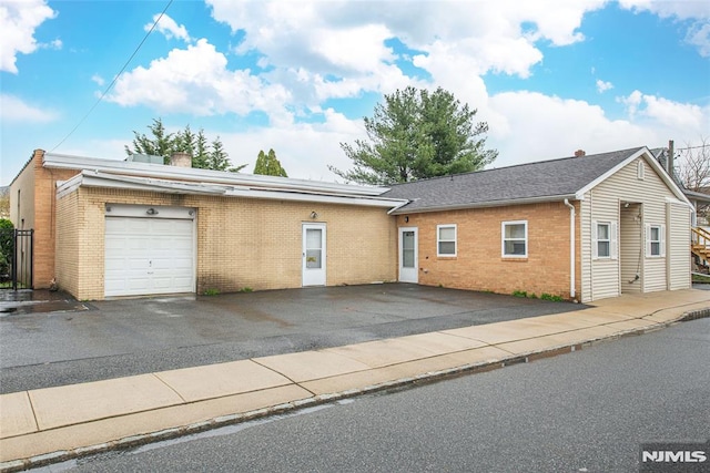 single story home featuring a chimney, driveway, a garage, and brick siding