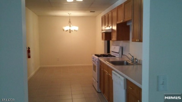 kitchen with white appliances, under cabinet range hood, hanging light fixtures, brown cabinets, and a notable chandelier