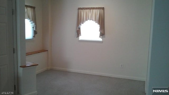 spare room featuring light colored carpet, baseboards, and a wealth of natural light