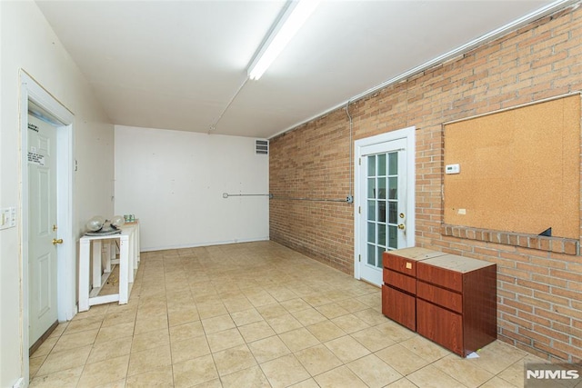 spare room featuring brick wall, visible vents, and light tile patterned flooring