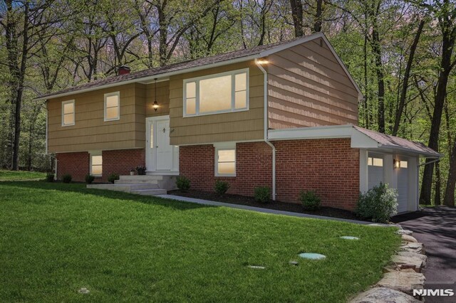 raised ranch featuring brick siding, a garage, a front lawn, and aphalt driveway