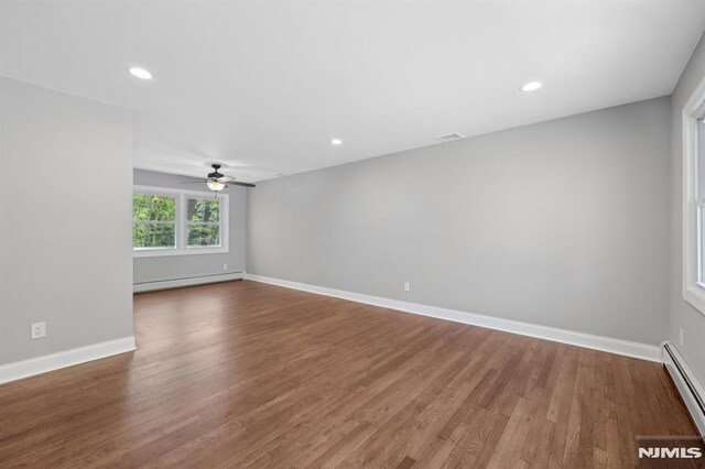 unfurnished room with baseboards, ceiling fan, wood finished floors, and baseboard heating