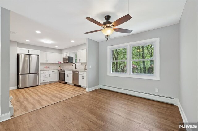 kitchen featuring ceiling fan, appliances with stainless steel finishes, baseboard heating, white cabinets, and light wood-style floors