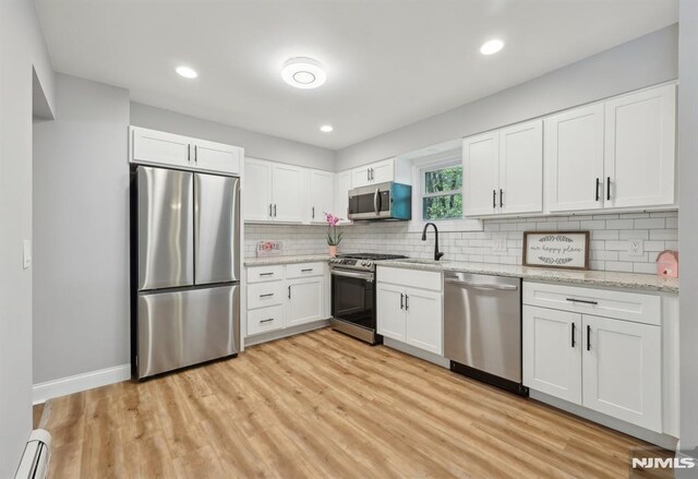 kitchen featuring backsplash, appliances with stainless steel finishes, light wood-type flooring, a baseboard radiator, and white cabinets