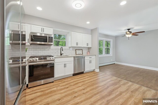 kitchen with decorative backsplash, white cabinetry, a baseboard heating unit, a sink, and stainless steel appliances