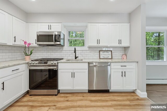 kitchen with a sink, appliances with stainless steel finishes, a baseboard heating unit, and a healthy amount of sunlight