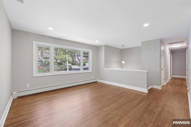 empty room featuring wood finished floors, baseboards, attic access, recessed lighting, and a baseboard radiator