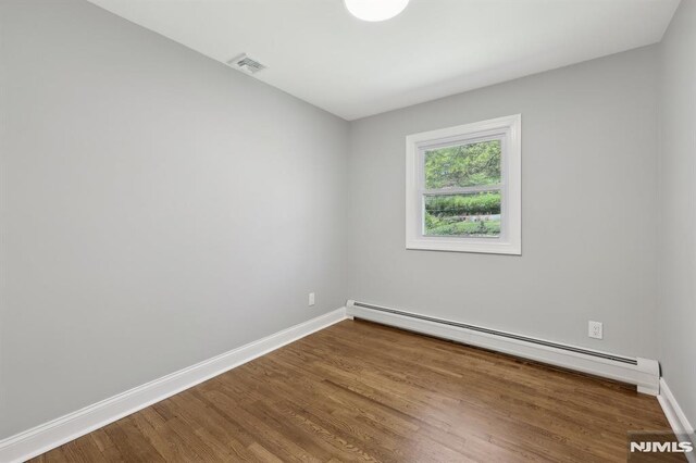 unfurnished room with baseboards, visible vents, wood finished floors, and a baseboard radiator