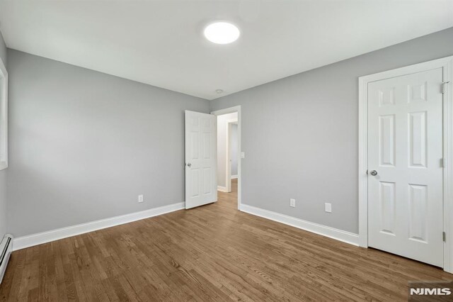 unfurnished bedroom featuring baseboards, a baseboard heating unit, and wood finished floors
