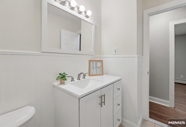half bathroom featuring a wainscoted wall, vanity, toilet, and wood finished floors
