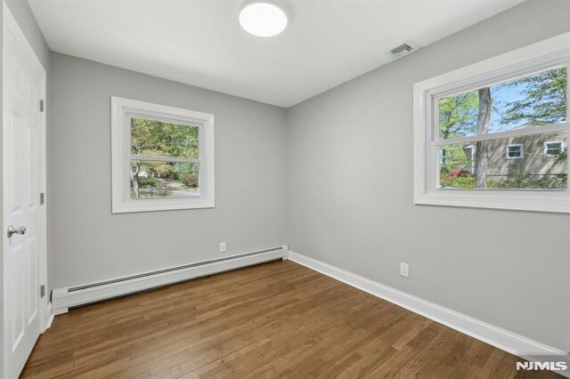 unfurnished bedroom featuring baseboards, a baseboard heating unit, and multiple windows