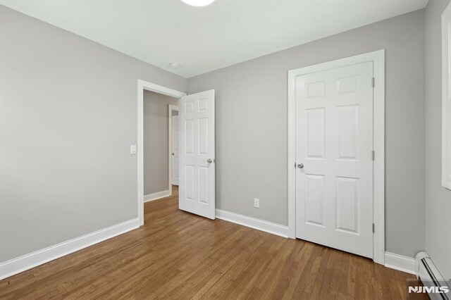 unfurnished bedroom featuring baseboards, baseboard heating, and wood finished floors