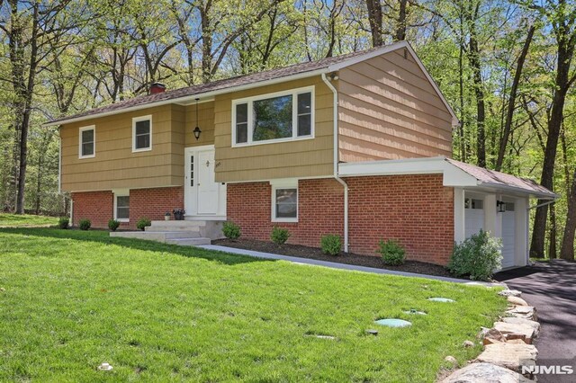 bi-level home featuring a front lawn, aphalt driveway, a garage, brick siding, and a chimney