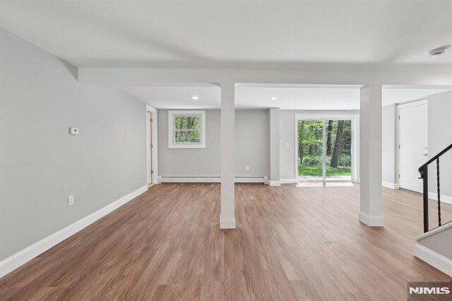 basement featuring baseboards, stairs, light wood-style flooring, and a wealth of natural light
