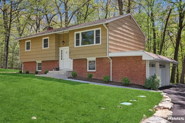 bi-level home featuring brick siding, a chimney, a front yard, and aphalt driveway